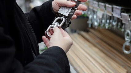 Focused worker gripping metallic carabiner, inspecting hardware details among shelves of...
