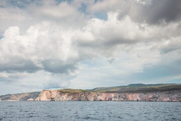 Breathtaking cliffs stretch along the coastline, their rugged beauty highlighted by soft clouds...