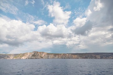 A breathtaking view of calm waters lapping against rugged cliffs, surrounded by dramatic, fluffy...