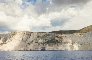 Soaring cliffs stand tall against a serene sea, captured during a calm day as clouds dance...
