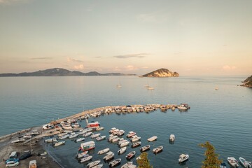 As the sun dips low, a gentle glow envelops a lively harbor brimming with various boats. Nearby...