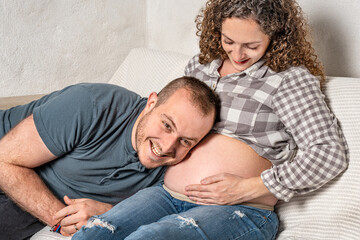 Happy husband listening to the baby inside the wife’s belly.
Joyful concept of maternity and parenting.