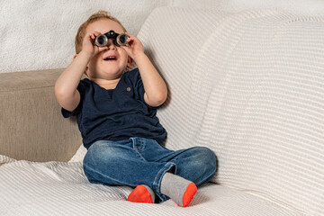 Toddler with tiny binoculars exploring his living room.
Amazed kid discovering his world more closely.