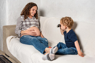 Curious son looking closely with binoculars at his mom’s pregnancy
An infant wants to know what sibling will come out of her mother.