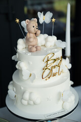 Two-Tiered White Cake with Buttercream, Cloud Decorations, and a Teddy Bear Figurine for a Baby Shower Celebration