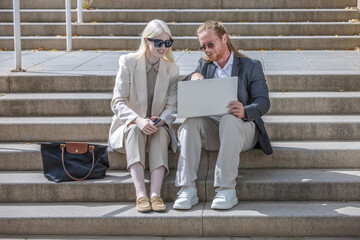 Business colleagues discussing project on laptop outdoors on steps