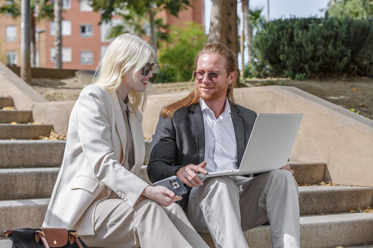 Albino woman and redhead man collaborate on laptop outdoors - Powered by Adobe