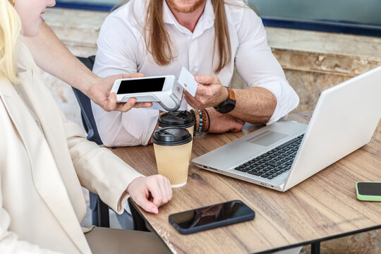 Businessman pays with credit card at cafe while working with colleague