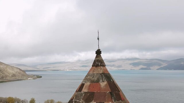 Aerial close up view top cupola and christian cross over Sevanavank Monastery and chapel overlooking famous Sevan lake at cloudy day. Tourist group visit.Travel and tourist destinations of Armenia