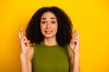 Hopeful young woman crossing fingers on yellow background for positivity and luck, casual fashion...