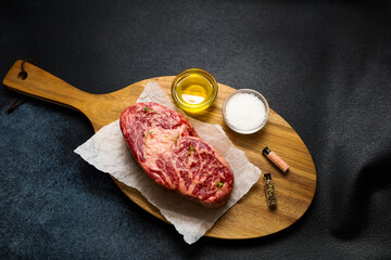 High quality marbled steak with olive oil and seasonings on a wooden cutting board