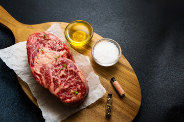 Freshly prepared steak with olive oil salt and spices on a wooden cutting board