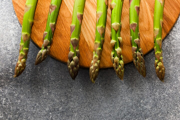 Fresh asparagus arranged on a wooden cutting board against a stone background