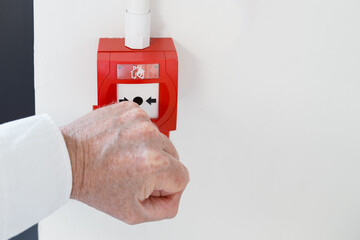 Office worker seen attempting to break the thin glass to activate a generic fire and smoke alarm seen within a commercial building. An emergency exit door is on the left of the image.