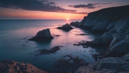 Sunset over coastal cliffs and rocks with calm waters and a colorful sky.