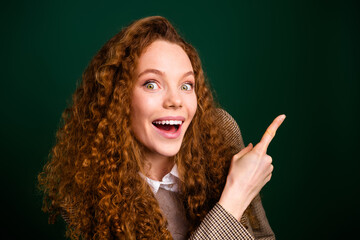 Excited red-haired woman pointing to the side on emerald background, showcasing joy and enthusiasm...