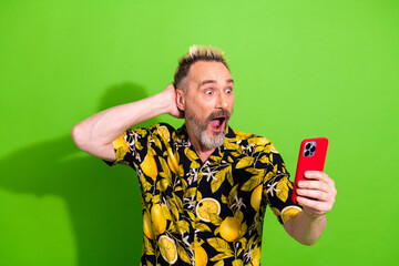 Charismatic middle aged man with funky blond hair holding a smartphone on a green background...