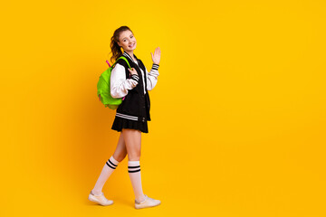 Smiling teenager wearing stylish varsity jacket with backpack standing on vibrant yellow...