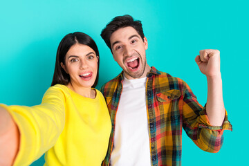 Obraz premium Excited young couple captures joyful selfie against a vibrant teal background conveying happiness and togetherness