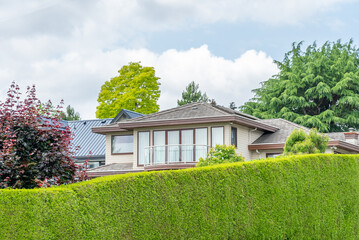 Top of grey stucco luxury house with shingle roof, green trees and nice windows in Spring in Vancouver, Canada, North America. Day time on May 2025.