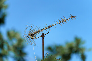 Antique television antenna mounted on a pole against a clear blue sky surrounded by green foliage