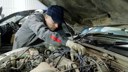 Skilled automotive technician wearing protective gloves, inspecting engine components and...
