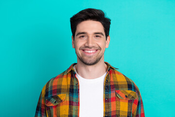 Cheerful young man in a colorful plaid shirt posing against a vibrant teal background with...