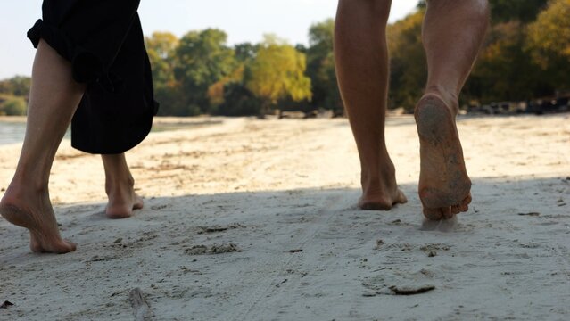 Male and female legs of pair walking on sandy beach. Bare feet of couple stepping along sand shore at sunny day. Lovers spending time together at resort. Concept of summer vacation or holiday