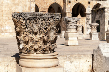 Close-up of intricately carved Corinthian column capitals in an ancient stone courtyard, showcasing...