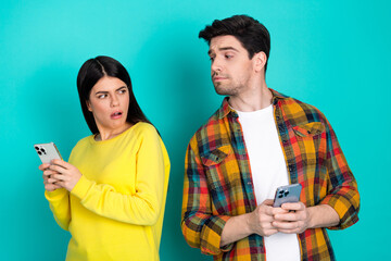 Young couple sharing an awkward moment while using smartphones against a turquoise background