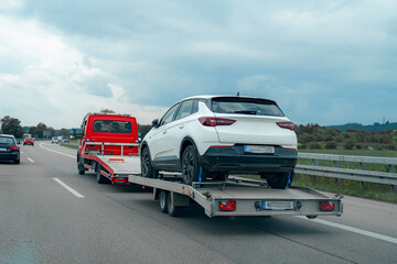 Vehicle transport on highway with white SUV on trailer behind red truck in overcast weather