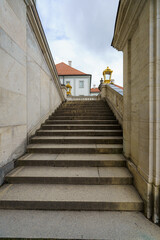 Obraz premium Stairs leading to an elegant building with a red roof and golden sculptures under a cloudy sky