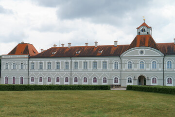 Historical building with clock tower and red roof located in a grassy landscape under gray clouds