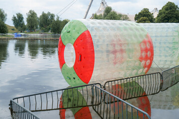 Floating water activity on a lake featuring a large inflatable rolling ball with colorful patterns...