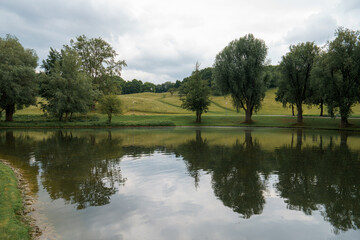 Calm river reflecting trees and hills on an overcast day in a serene park setting