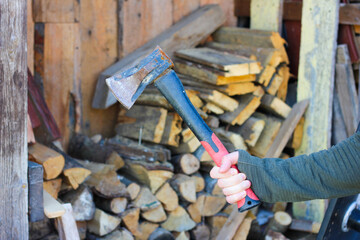 Hand Holding an Axe in Front of a Stack of Firewood
