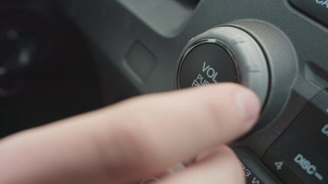 Close up of hand pressing volume push power knob then rotating dial to adjust audio settings on car stereo control panel capturing finger interaction with vehicle interior media interface