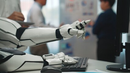 A robotic hand extends towards a keyboard in a modern office. Professionals engage in discussions,...