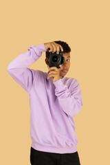 Vertical image of a dark skinned Latino teenager wearing a lilac sweatshirt holding a camera taking...