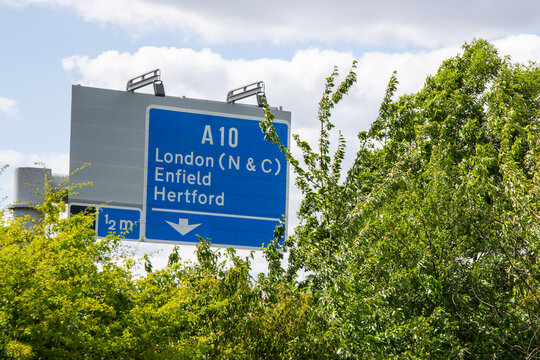 M25 motorway road sign for A10 slip road to London (N & C), Enfield, and Hertford, photographed through roadside foliage in summer.