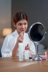 Woman applies makeup in front of mirror after her shower, focusing on skin care and enhancing her...