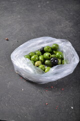 Green olives and black olives in a cellophane bag on a gray background