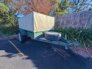 Photograph of an old rusty and dirty small sized trailer with a covered tray that is parked in a...