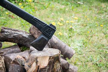 Outdoor scene with an axe embedded in a chopping block beside a pile of logs, suggesting rustic...