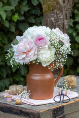 Blumenstrauß mit pink Rose, Pfingstrosen, Mohnkapseln und Gypsophila im rustikalen Krug