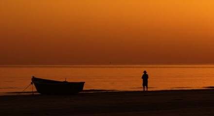 Fototapeta premium Sunset Solitude Fisherman by Boat at Golden Hour Beach.