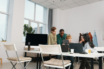 young adult woman and colleagues socializing and working together in a modern workplace, representing Gen Z friends collaborating on business tasks with laptops and digital devices