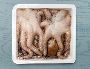 Vacuum-sealed frozen octopus in  white plastic tray  isolated on blue table with clipping path included