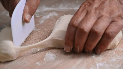 Close-up of artisan hands skillfully dividing fresh dough on a rustic wooden countertop in a warm kitchen environment