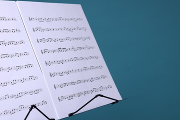 Note stand with music sheets on light blue background, closeup. Space for text